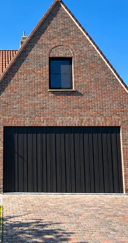 Zwarte sectionaalpoort met verticale profilering in een gevel van rode baksteen