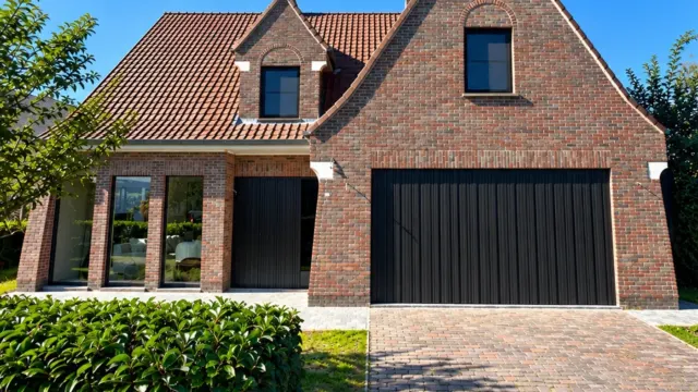 Landelijke woning in rode baksteen met zwarte garagepoort en zwarte ramen